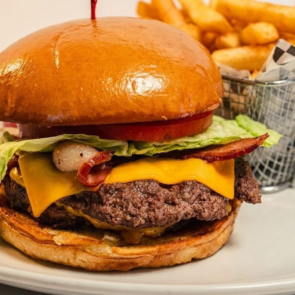 A juicy bacon cheeseburger with lettuce, tomato, and onions, served with a side of golden fries.