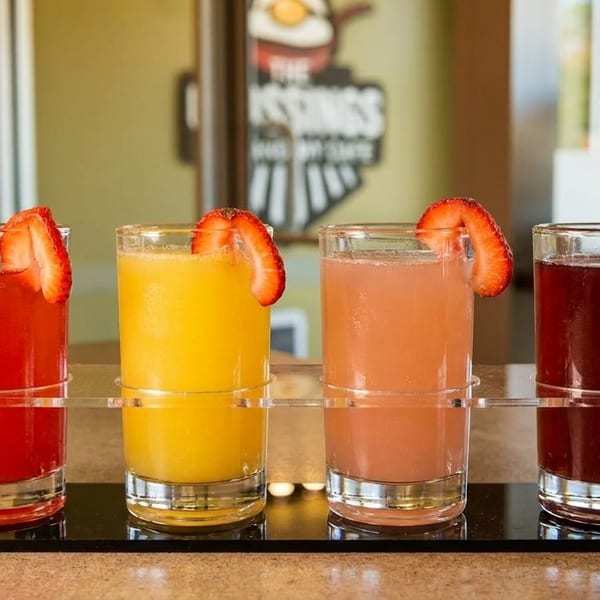 Four colorful juice drinks, garnished with strawberry slices, in a black serving tray.